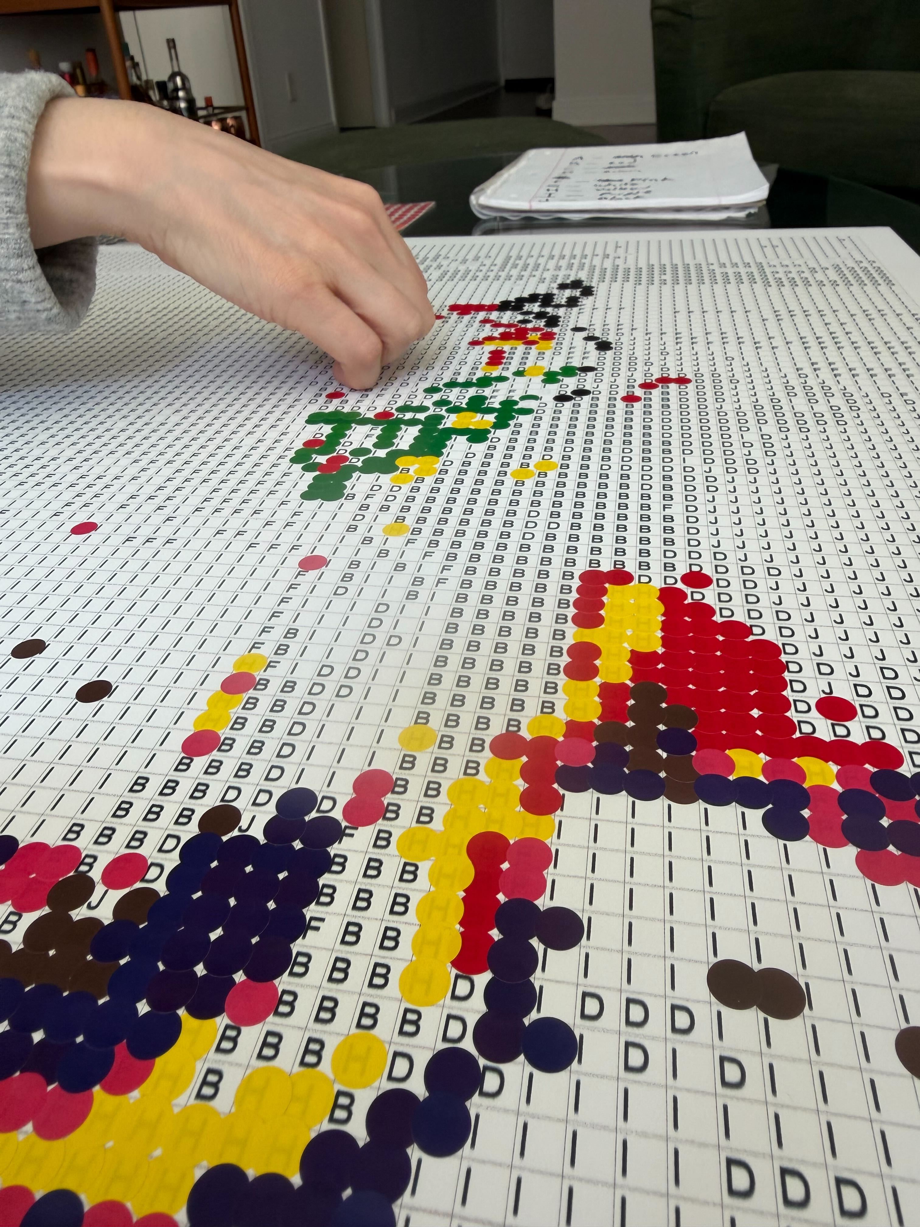 A Color A Dog kit mid-build — a hand placing colored dot stickers onto the numbered grid.